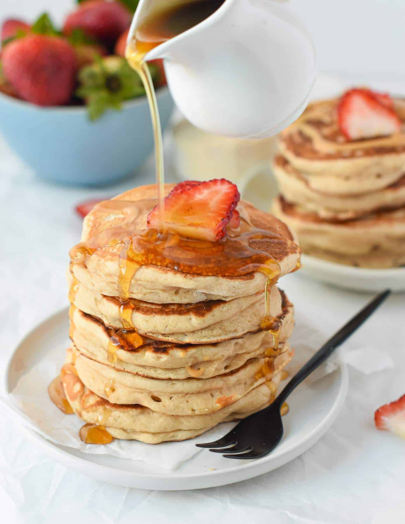 Vegan Protein pancakes stacked on a plate with a drizzle of maple syrup and a slice of strawberry.