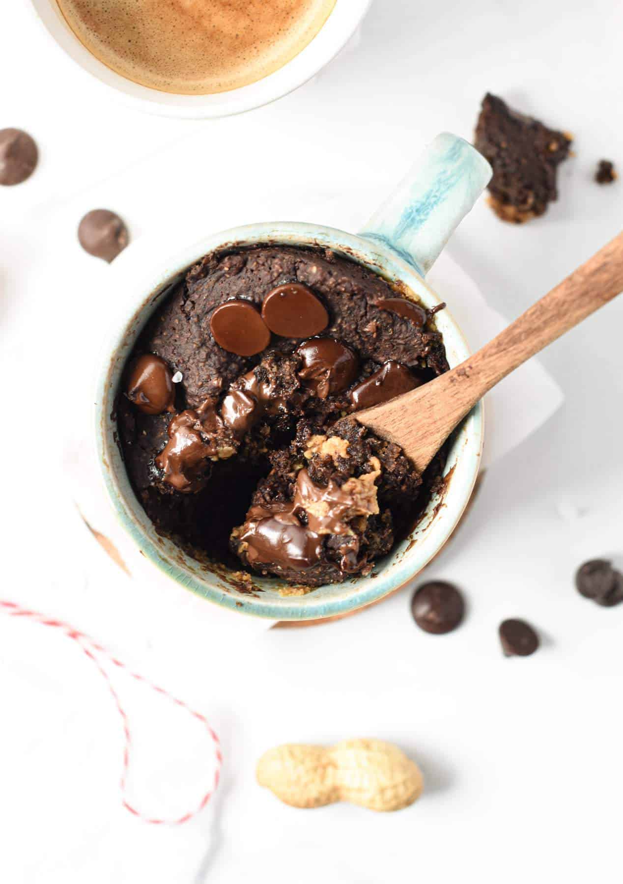 Protein Powder Mug Cake in a small mug decorated with chocolate chips with a small wooden spoon.