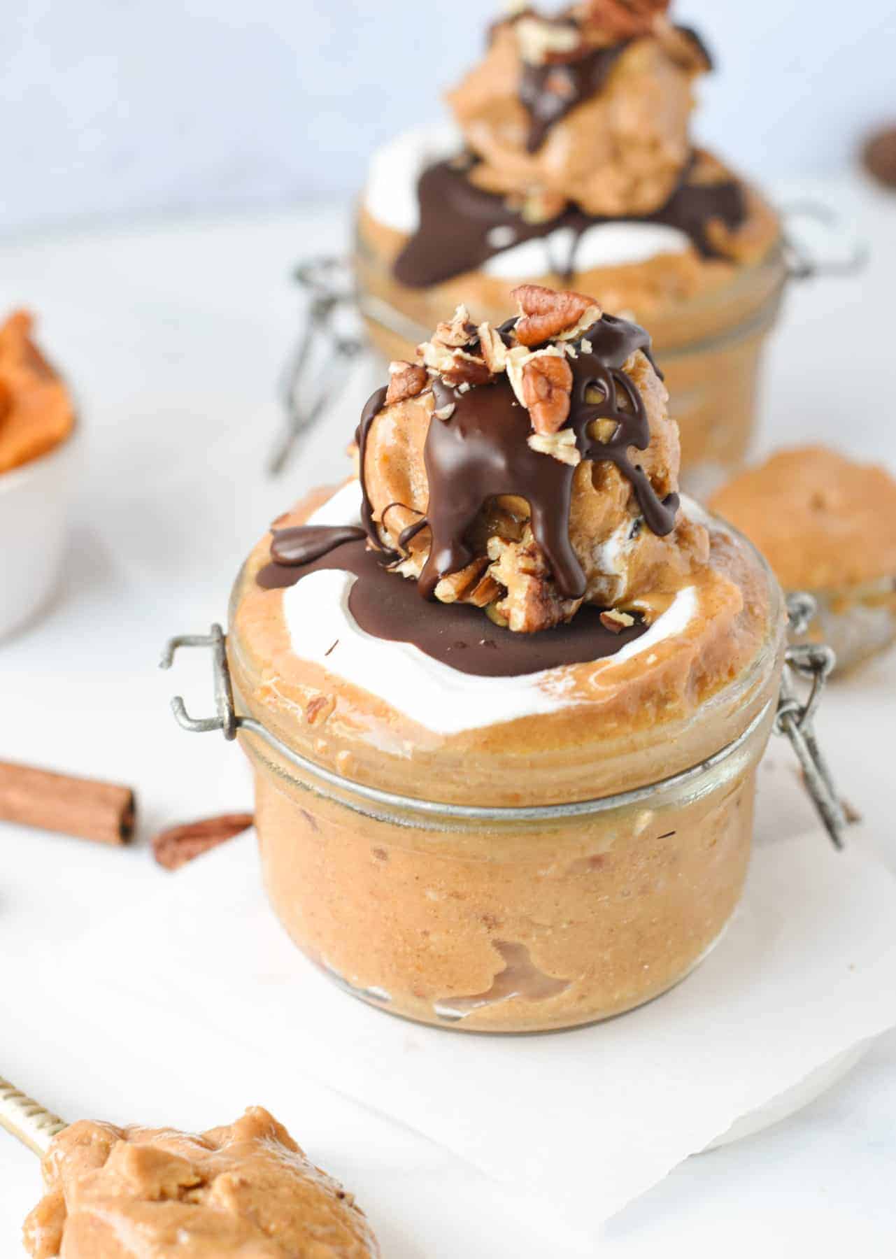 Pumpkin Nice Cream in a small jar, decorated with vegan yogurt, chocolate, and pecans.