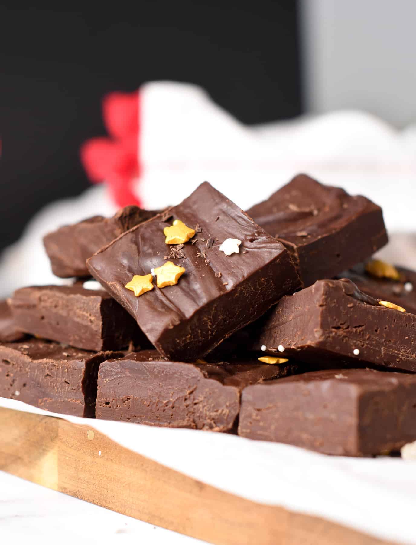2-Ingredient Fudge Recipe cut into squares, stacked on a wooden chopping board, and decorated with golden sprinkles.
