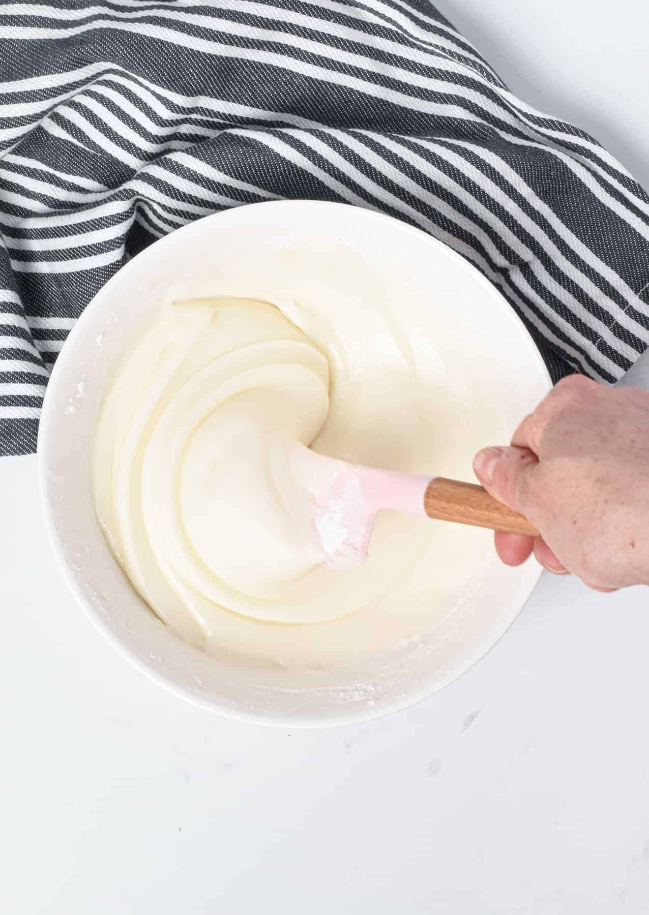 Vegan Royal Icing in a large bowl being stirred with a silicone spatula.
