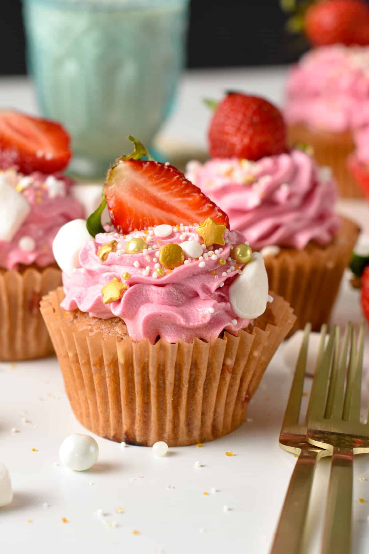 Vegan Strawberry Cupcakes decorated with pink frosting, fresh strawberries, and golden sprinkles.