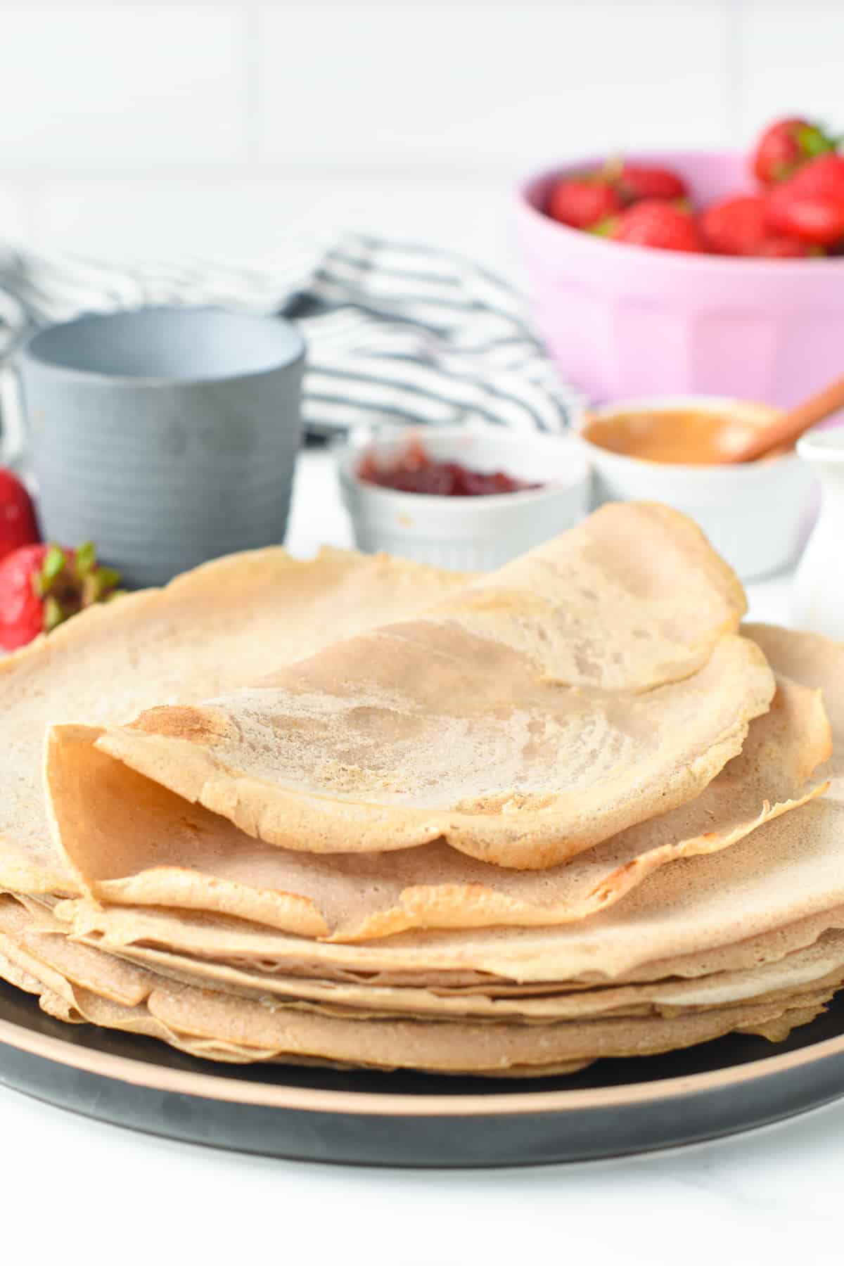 Vegan Buckwheat Crepes stacked on a black plate with the top one folded.