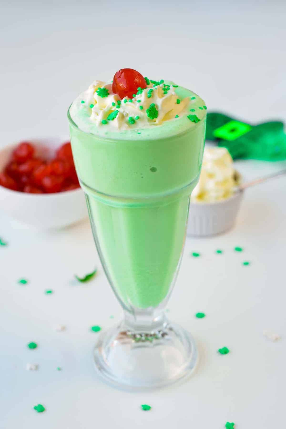 A glass with Vegan Shamrock Shake decorated with green sprinkles and glaceed cherry.