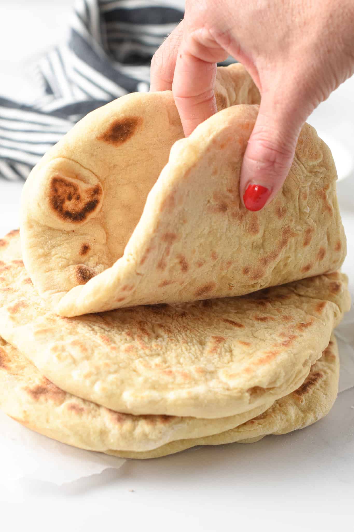 Holding a 2-ingredient Flatbread above a stack of bread.