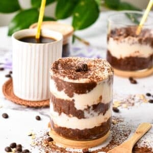 a glass jar filled with layers of chocolate coffee overnight oats, yogurt, and topped with a dust of cocoa to look like a tiramisu