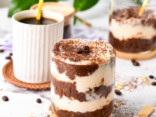 a glass jar filled with layers of chocolate coffee overnight oats, yogurt, and topped with a dust of cocoa to look like a tiramisu