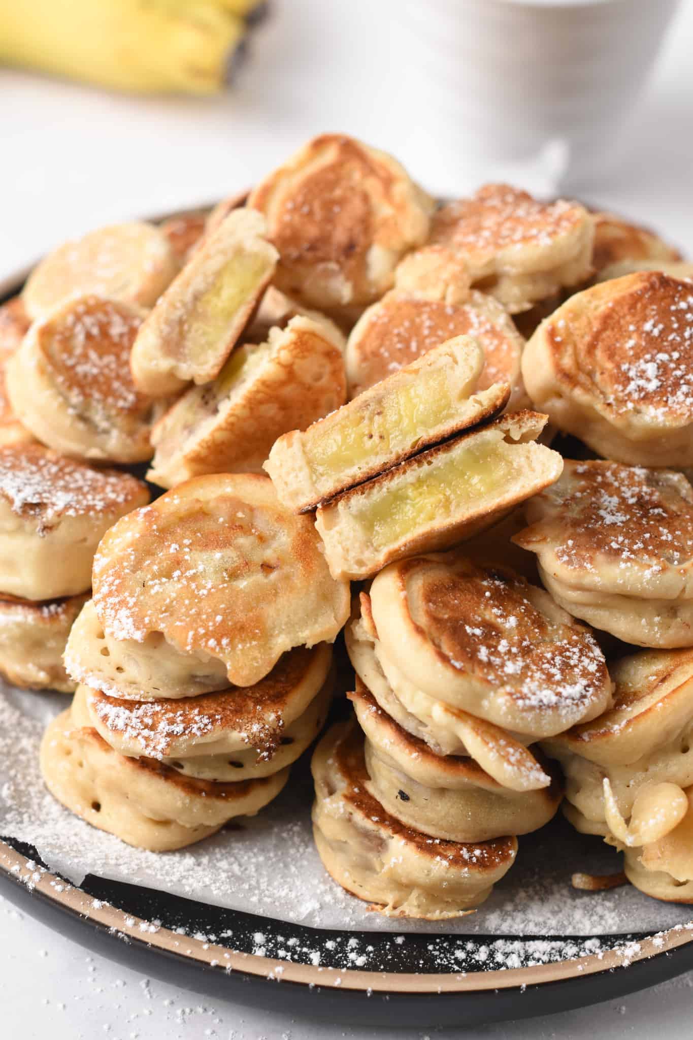 Dozens of Banana Pancake Bites stacked on a plate and decorated with powdered sugar.