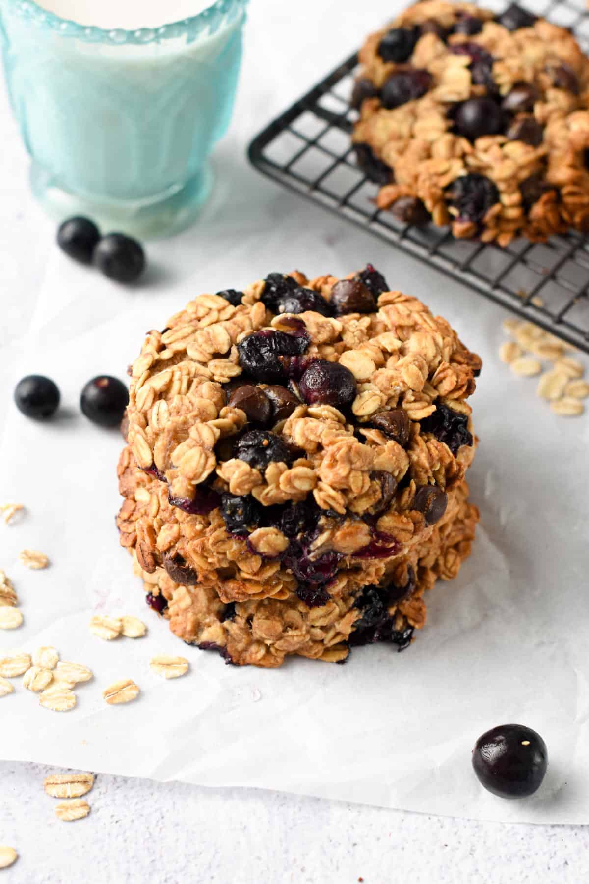 Blueberry Oatmeal Cookies stacked on a table next to a cooling rack.