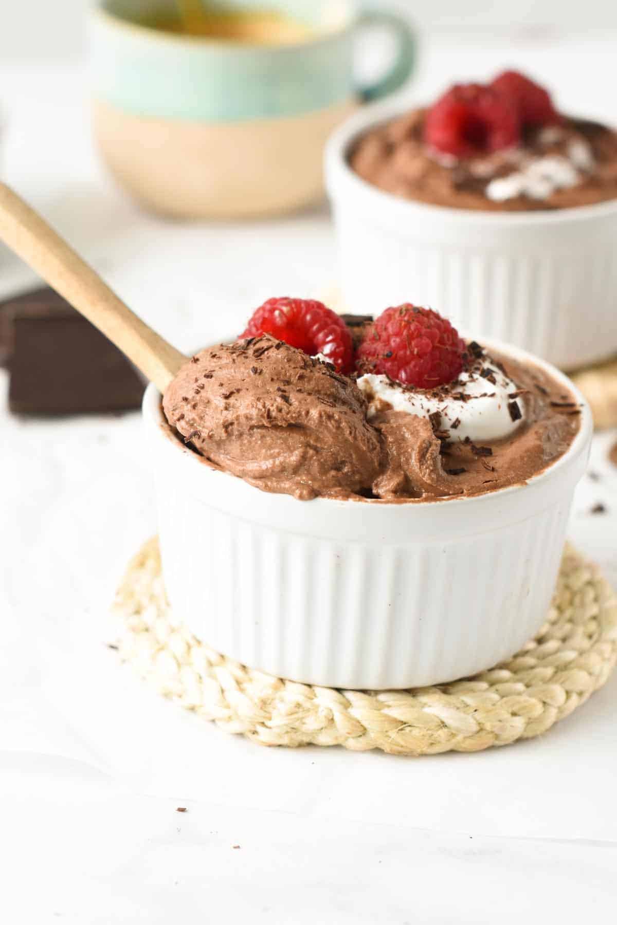 Tofu Mousse in a small white ramekin with fresh raspberries and a wooden spoon.