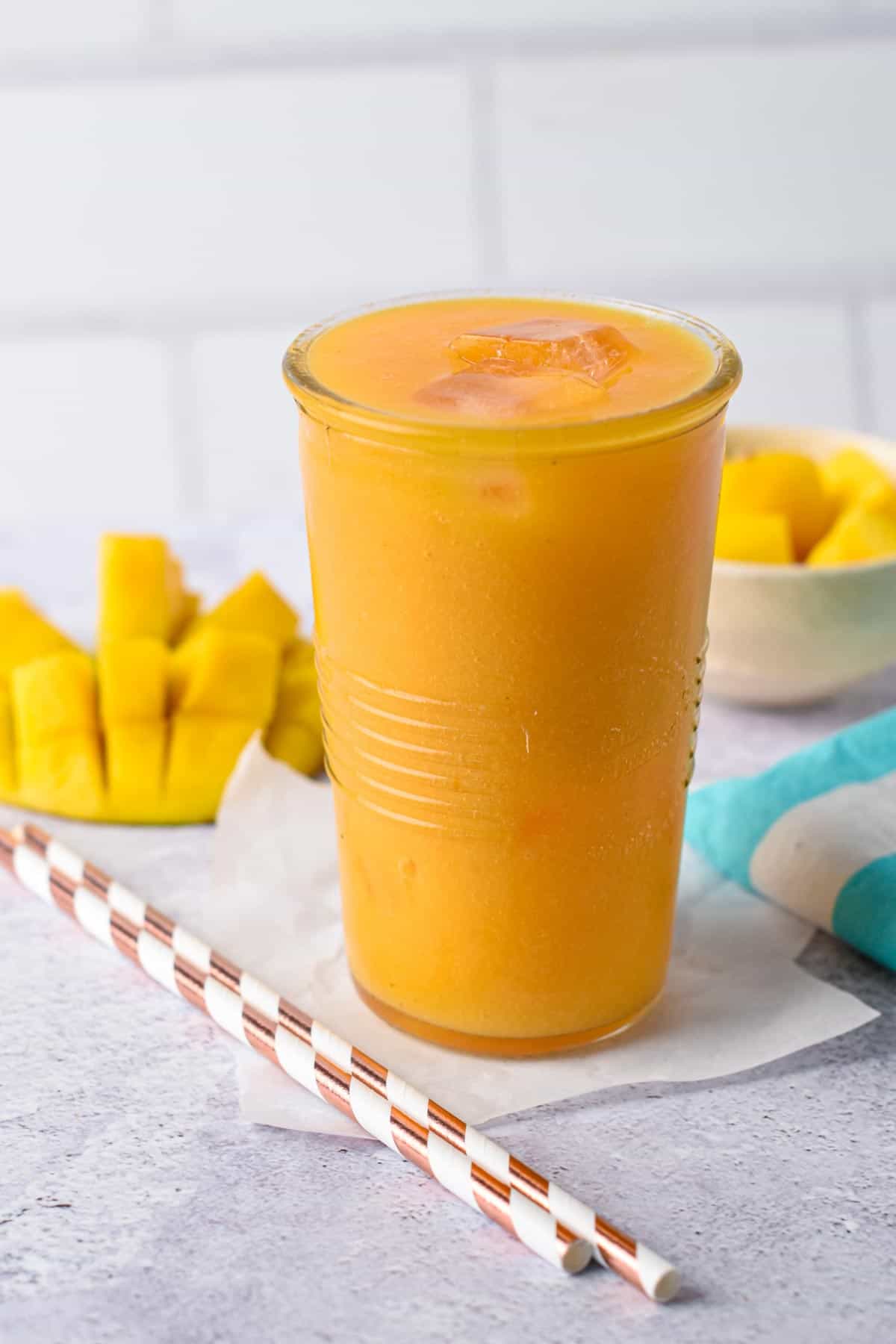 Mango Juice in a tall glass next to a fresh mango.