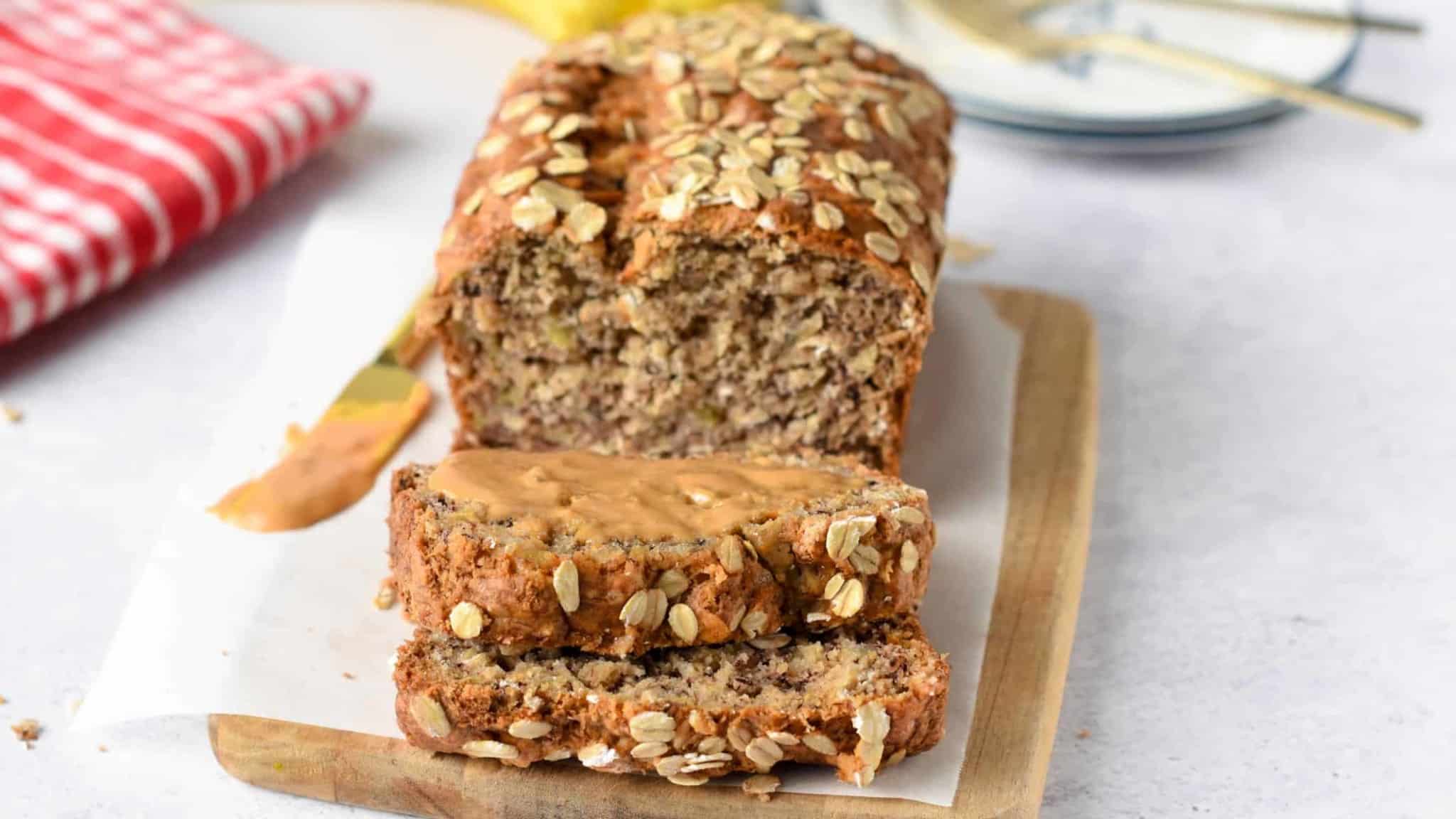 Banana Oatmeal Bread sliced on a chopping board with peanut butter on a slice.