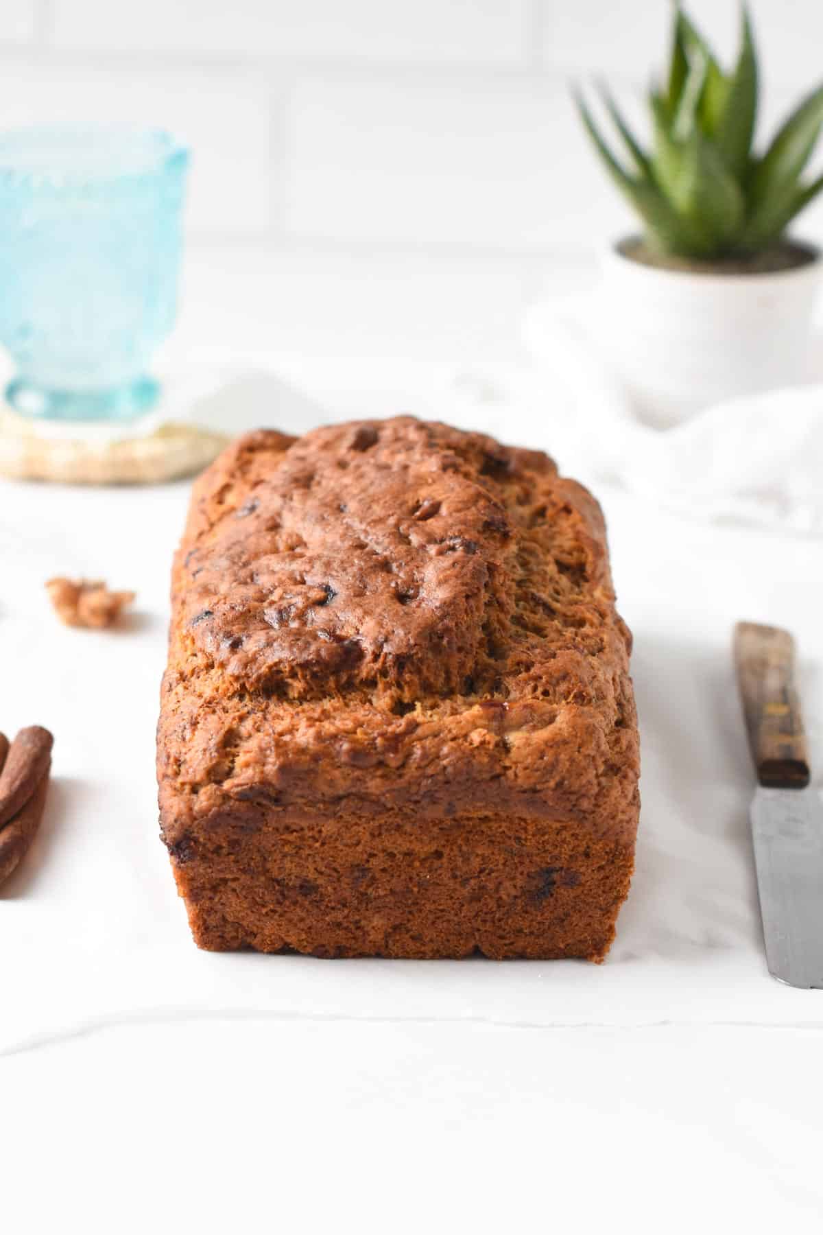 Eggless Banana Bread loaf on a white table with a small bread knife next to it.