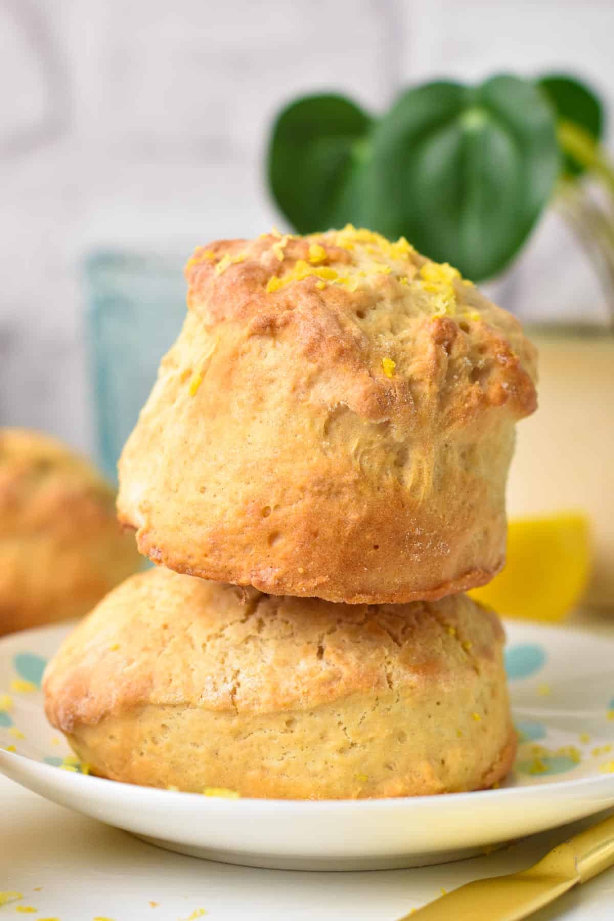 A stack of two ultra thick and fluffy lemonade scones with lemon zest on top and green plant in the background.