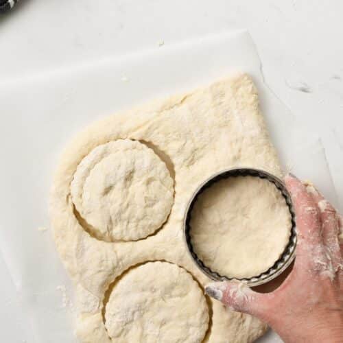 a scone dough rolled on a floured surface and a hand cutting scone shapes using a round scone cutter