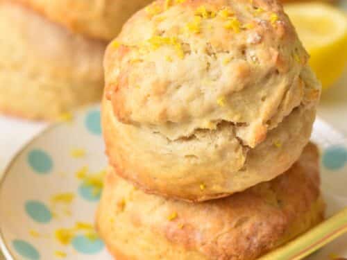a stack of two ultra thick and fluffy lemonade scones with lemon zest on top and lots of scones in the background