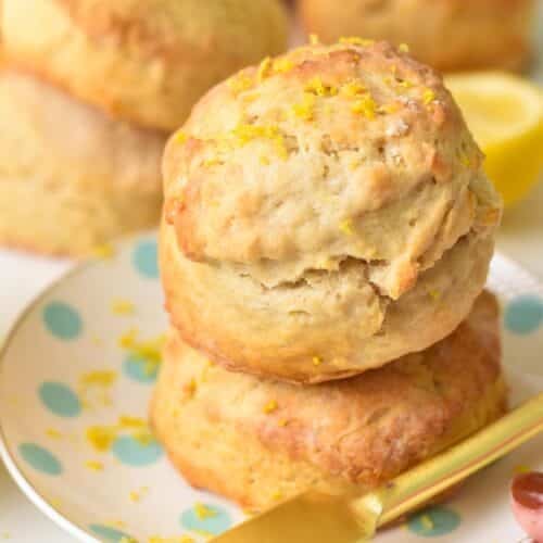 a stack of two ultra thick and fluffy lemonade scones with lemon zest on top and lots of scones in the background