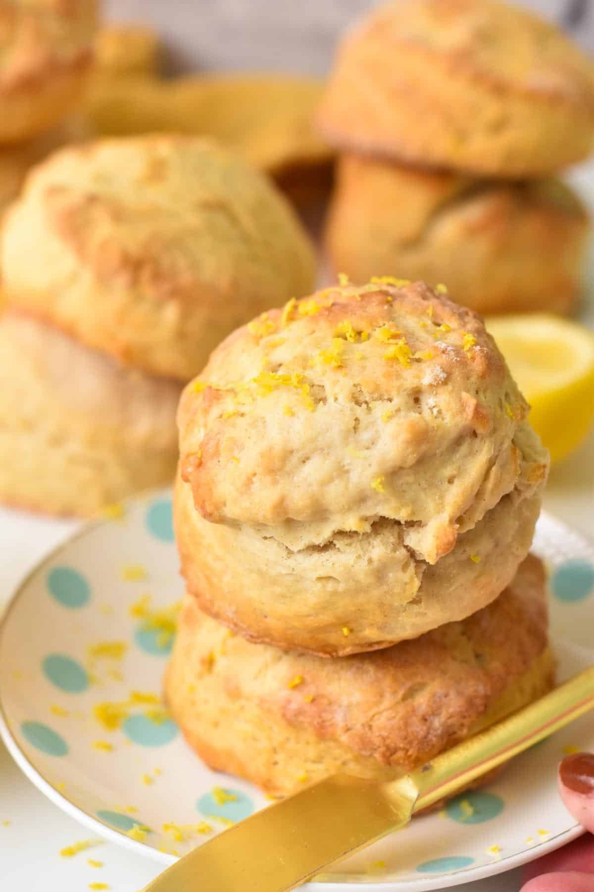 A stack of two ultra thick and fluffy lemonade scones with lemon zest on top and lots of scones in the background.