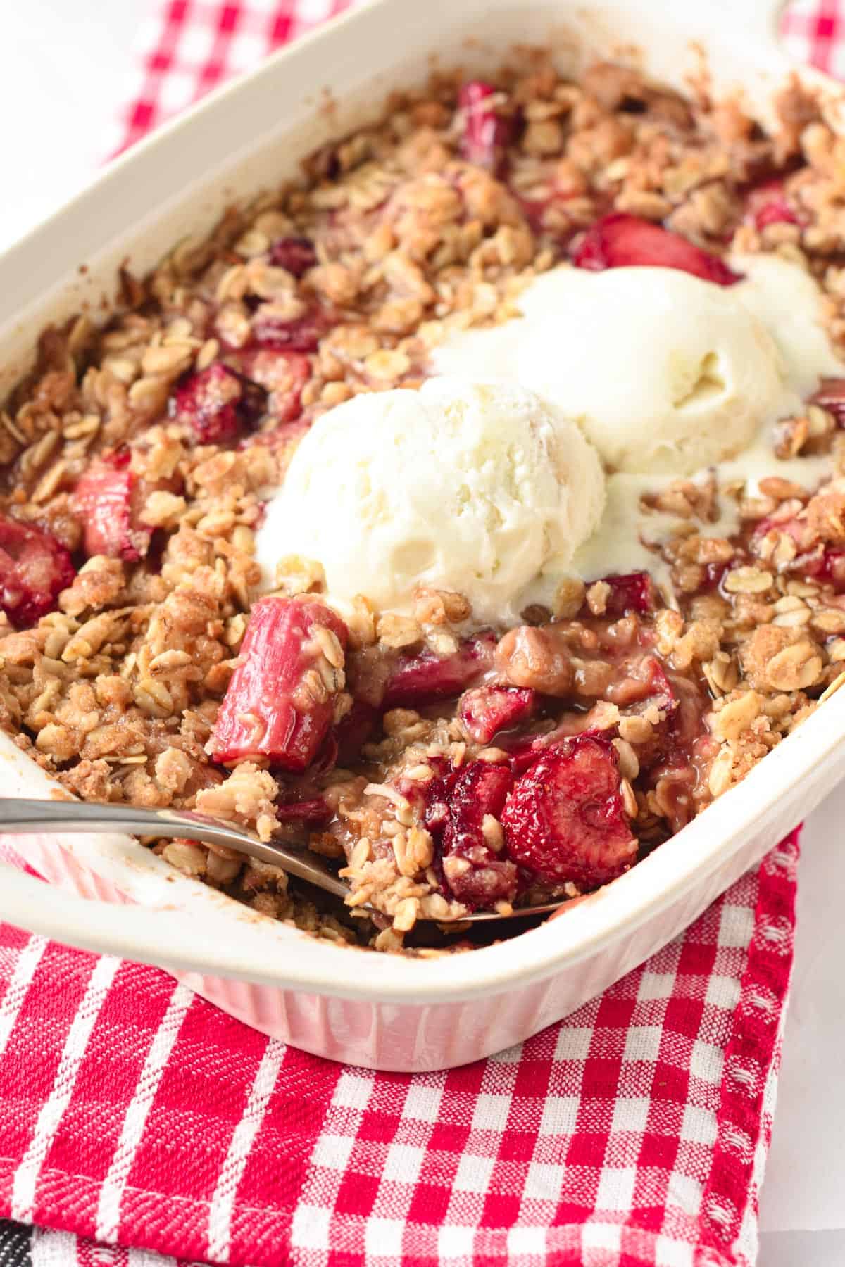 Strawberry Rhubarb Crisp in a ceramic pan with vegan ice cream scoops on it.