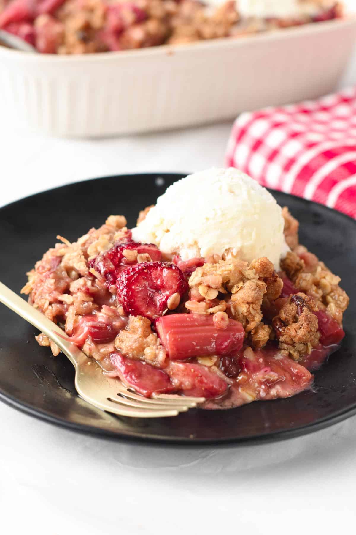 Strawberry Rhubarb Crisp portion on a place with a scoop of ice cream.