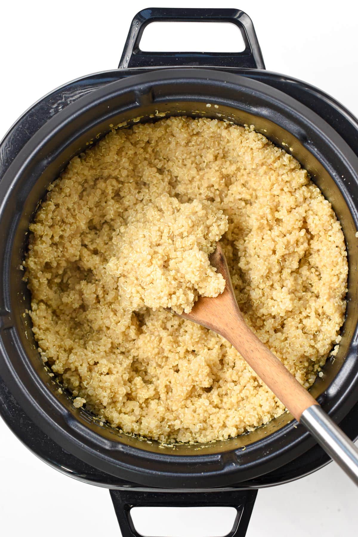 Quinoa cooking in a rice cooker with a wooden spoon.