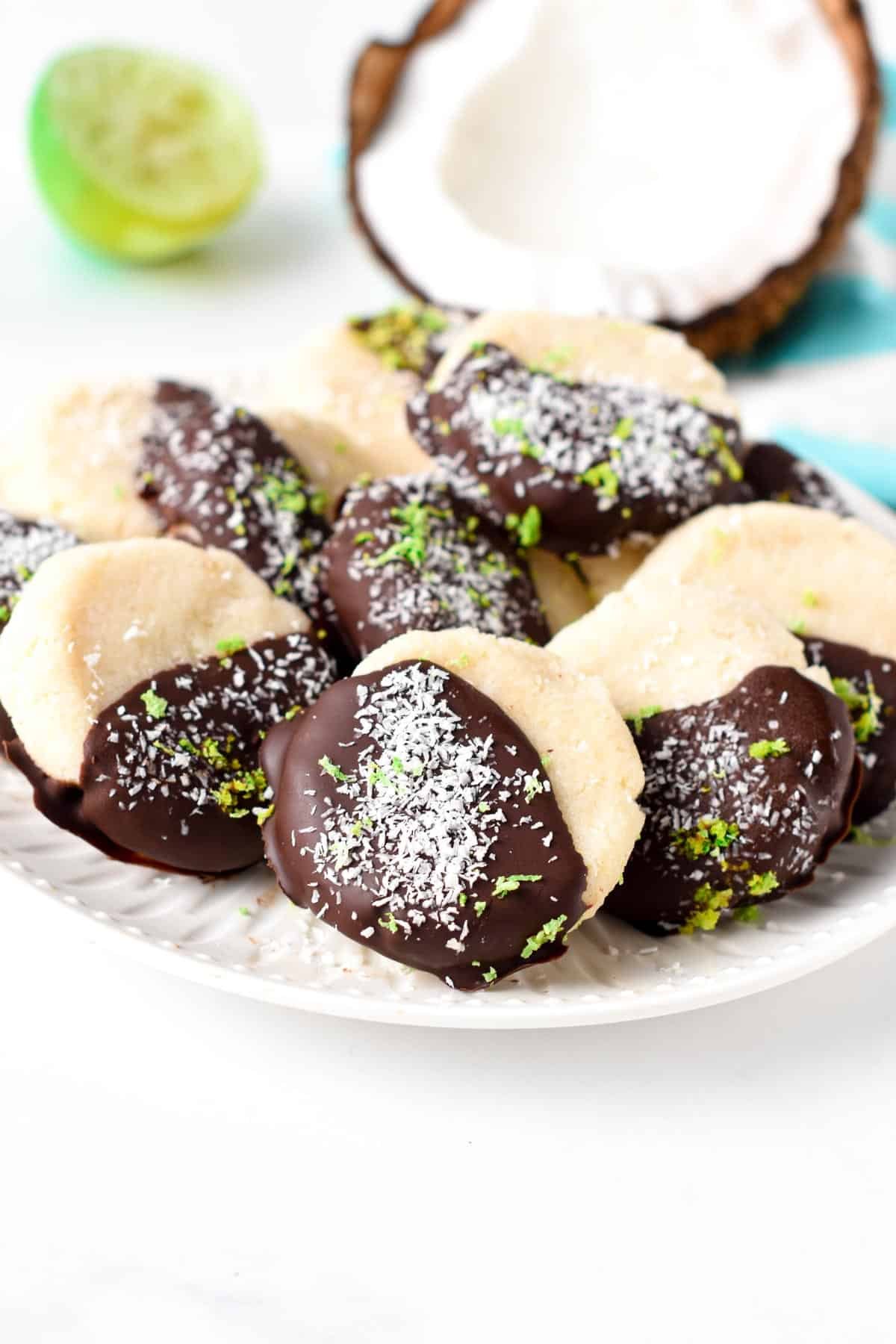 No-Bake Coconut Cookies decorated with chocolate, lime zest, and shredded coconut on a white plate.