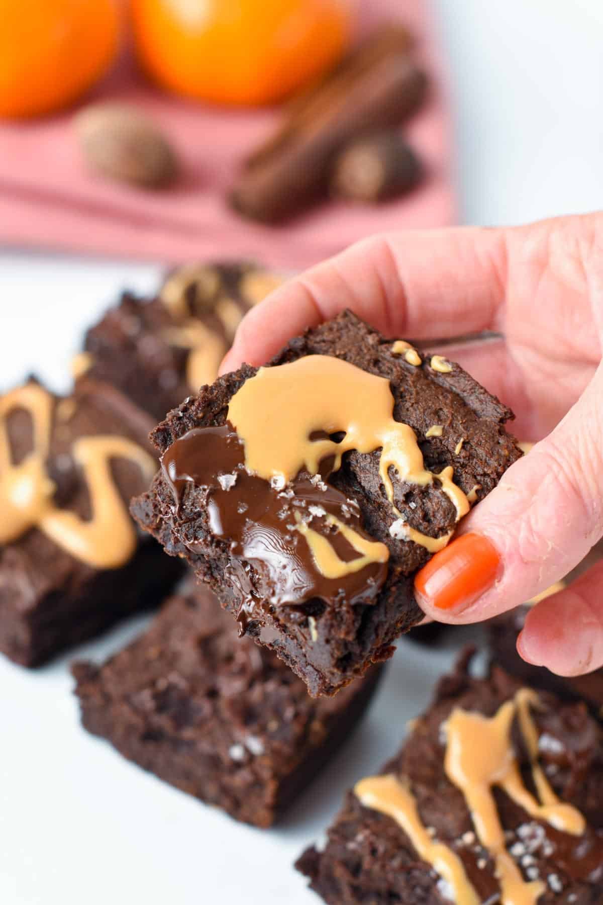 A square of Pumpkin Brownies held in a hand and covered with melted chocolate and peanut butter.