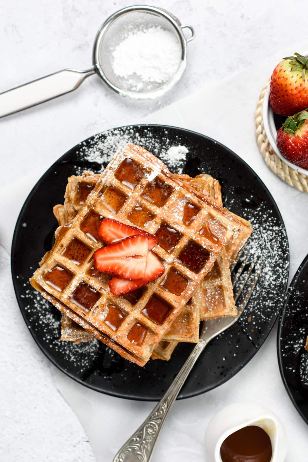 Buckwheat Waffles on a black plate, decorated with powdered sugar.