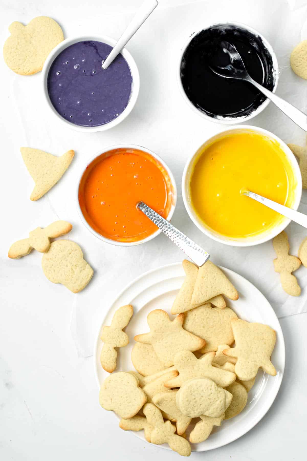 Undecorated Halloween Sugar Cookies with four ramekins with food coloring icing.