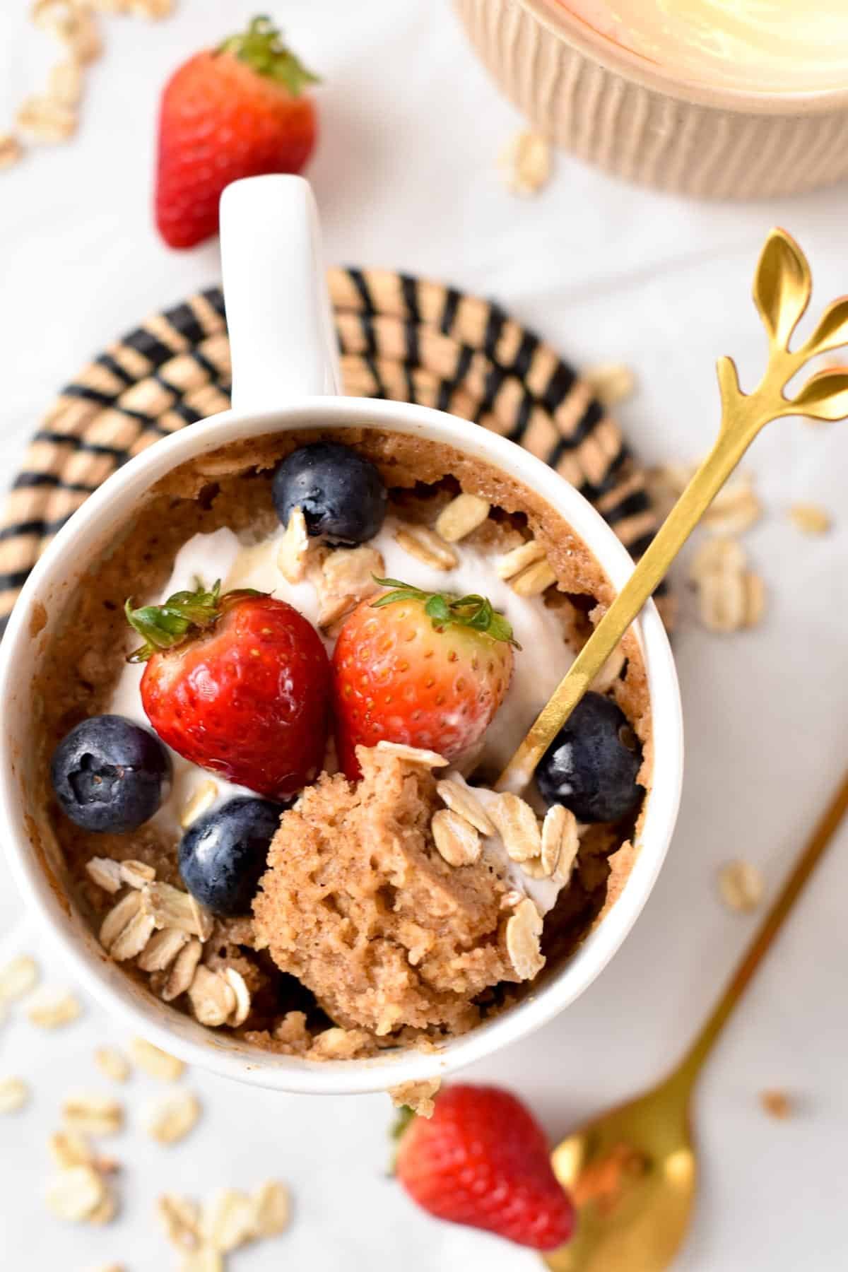 Oatmeal Mug Cake decorated with fresh berries and with a golden spoon.