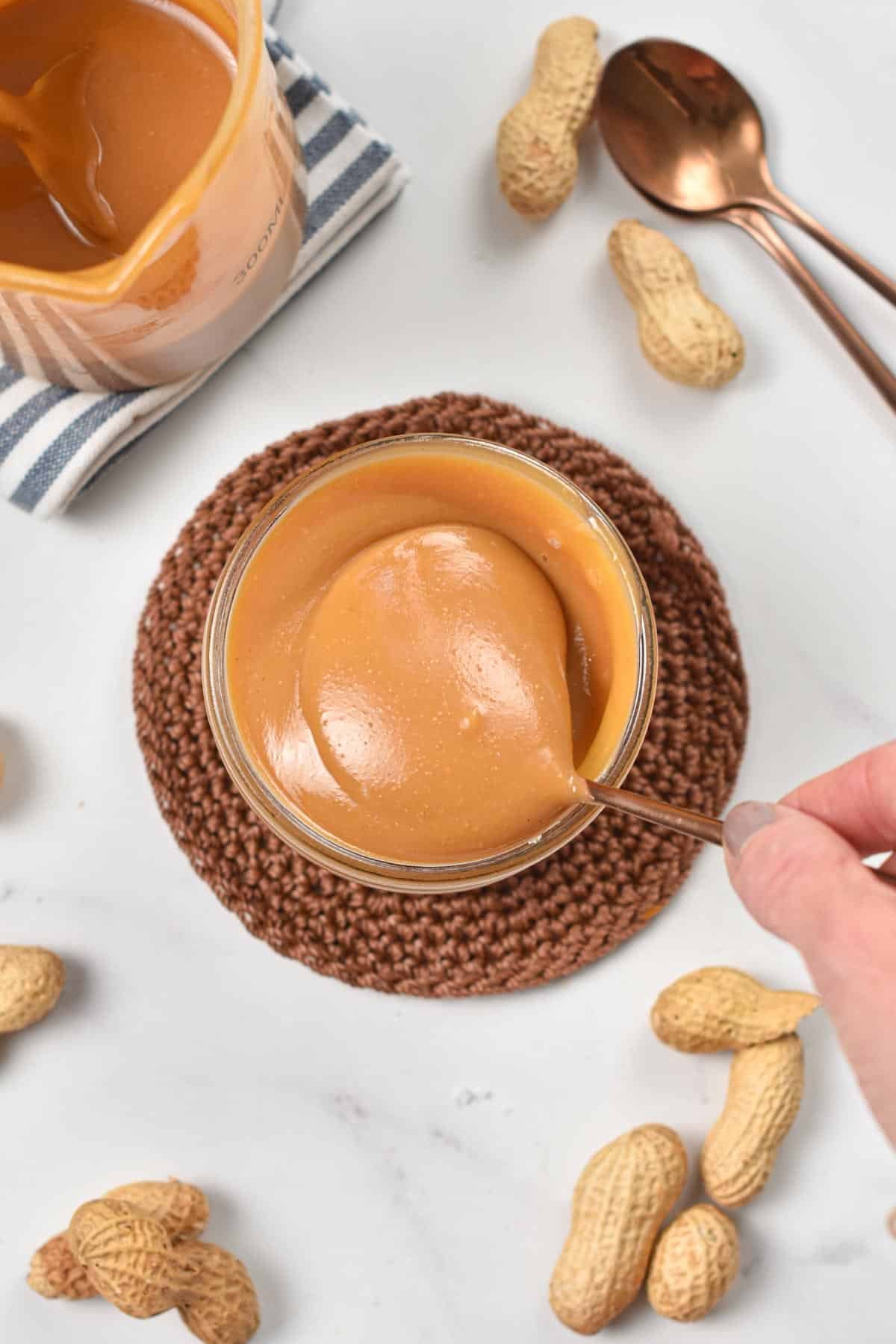 Peanut Butter Caramel Sauce in a glass jar with a golden spoon.