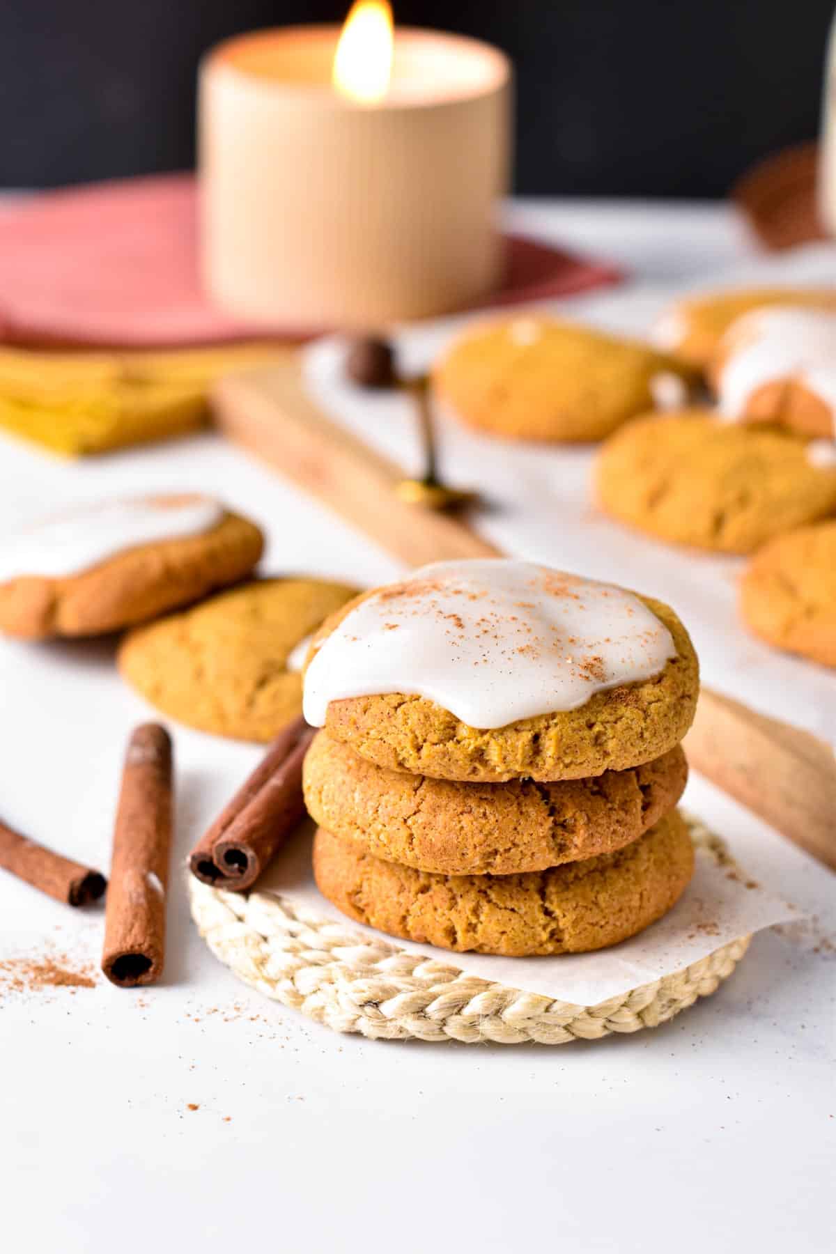Vegan Pumpkin Cookies decorated with icing, in front of a candle and next to cinnamon sticks.