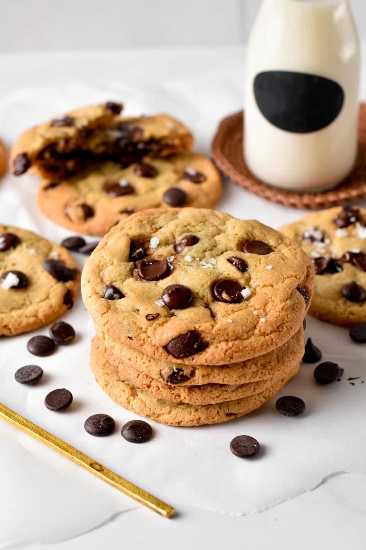 A stack of vegan chocolate chip cookies with a pinch of sea salt flakes on top, in front of a jar of plant-based milk.