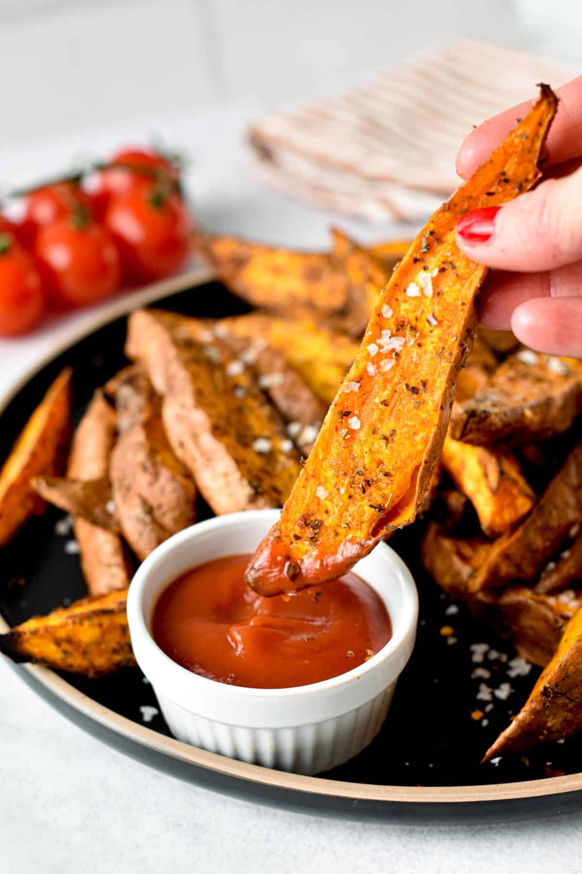 Dipping an Air Fryer Sweet Potato Wedge into a ramekin of ketchup.