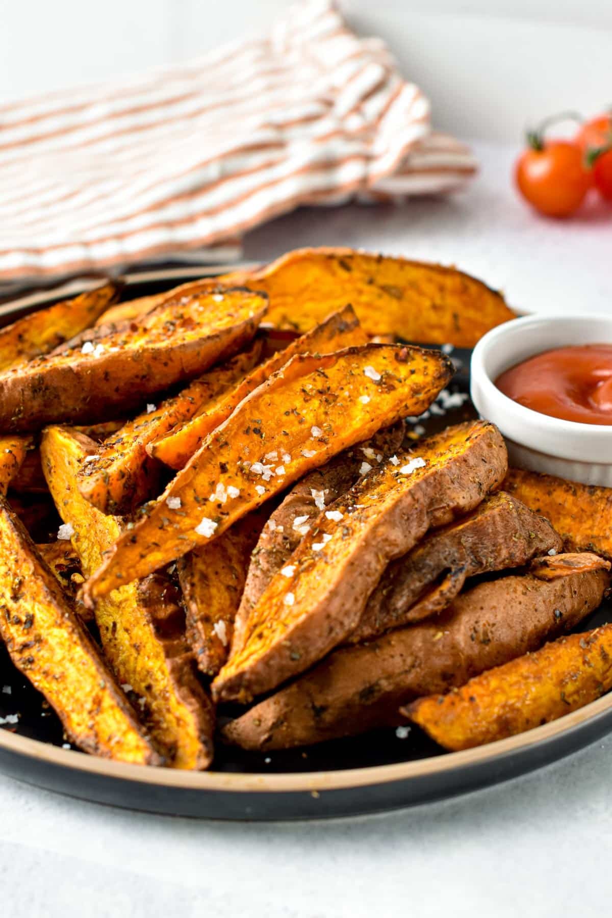 Air Fryer Sweet Potato Wedges on a black plate with a ramekin full of ketchup.