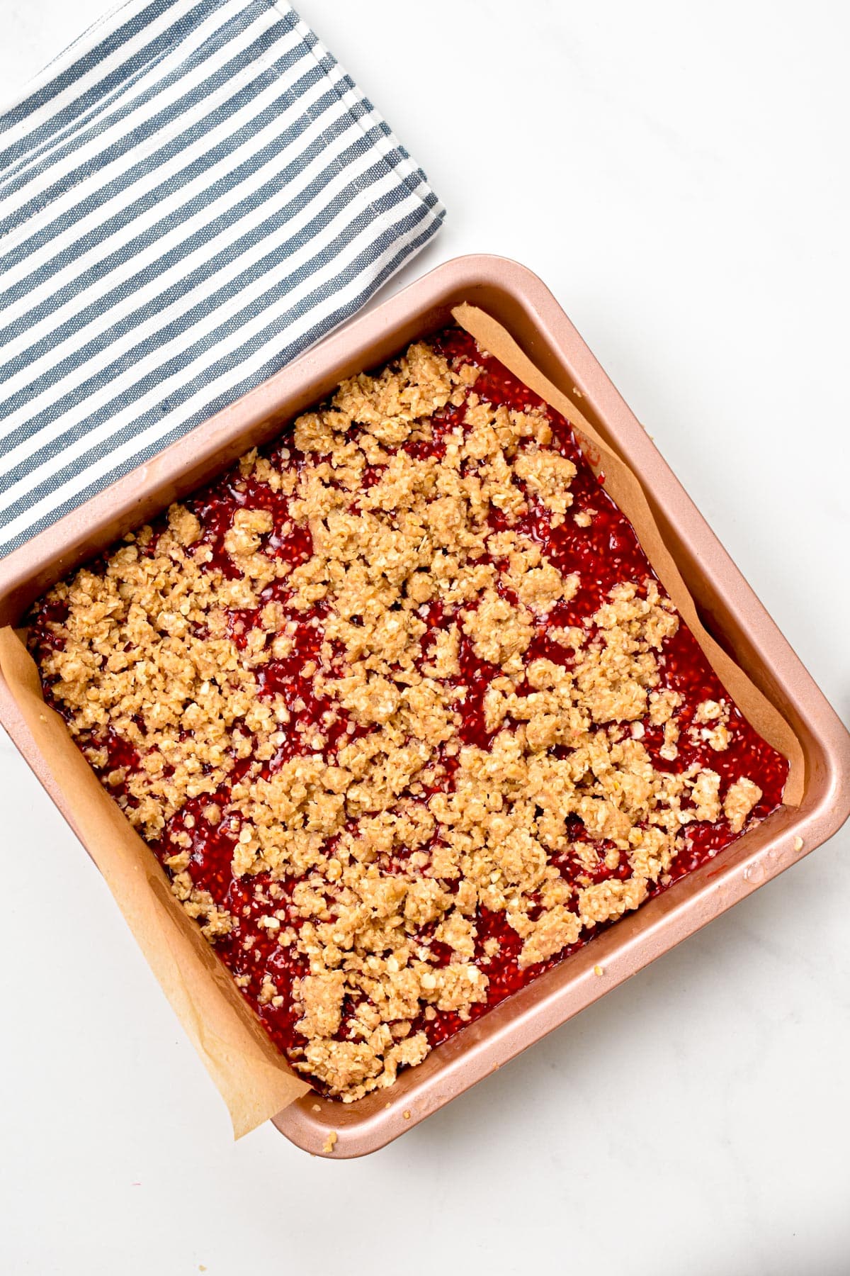 A Raspberry Oat Bars before baking in a pink 8 inches square pan lined with brown parchment paper.