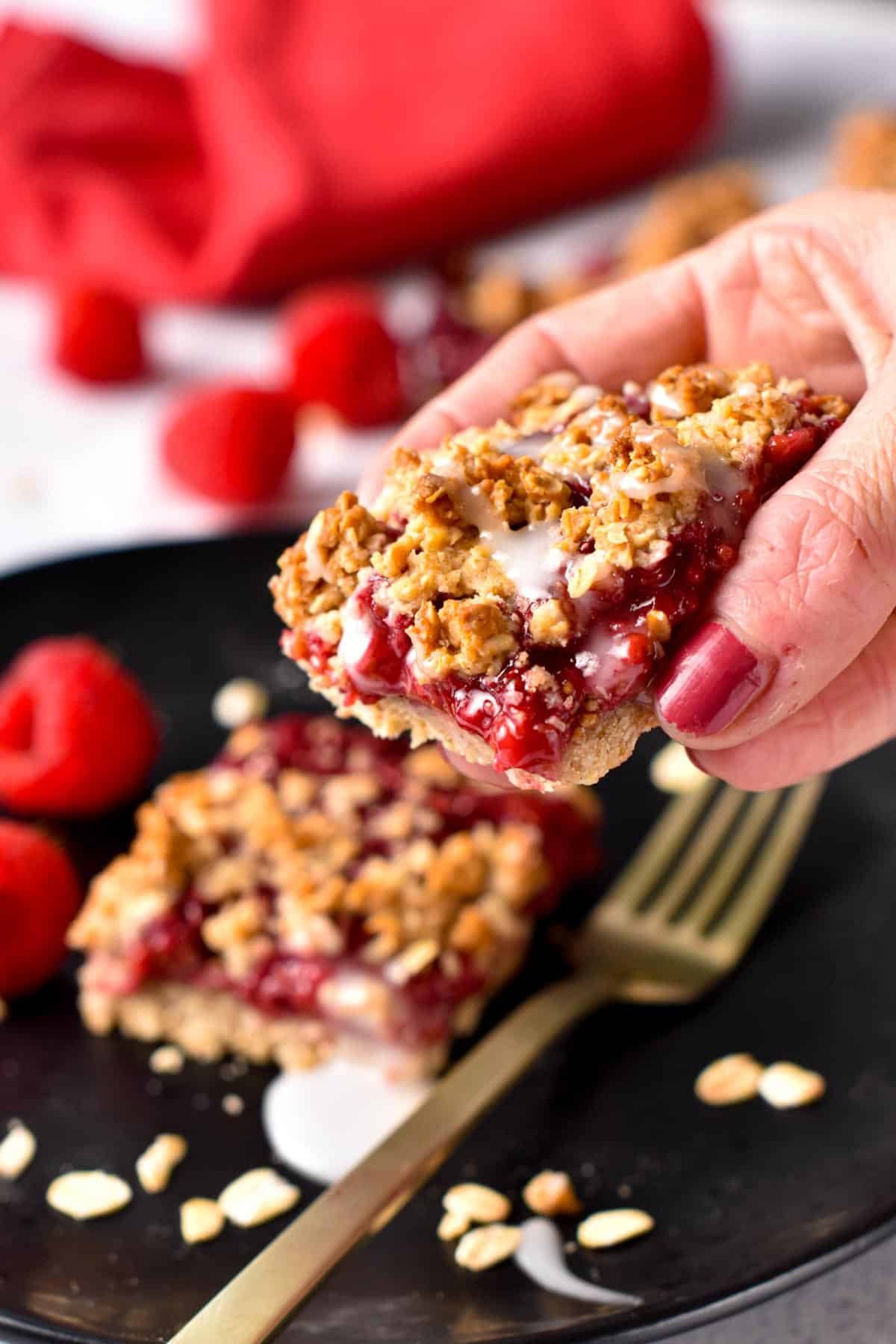 Raspberry Oat Bars lifted from a black plate with a golden spoon.