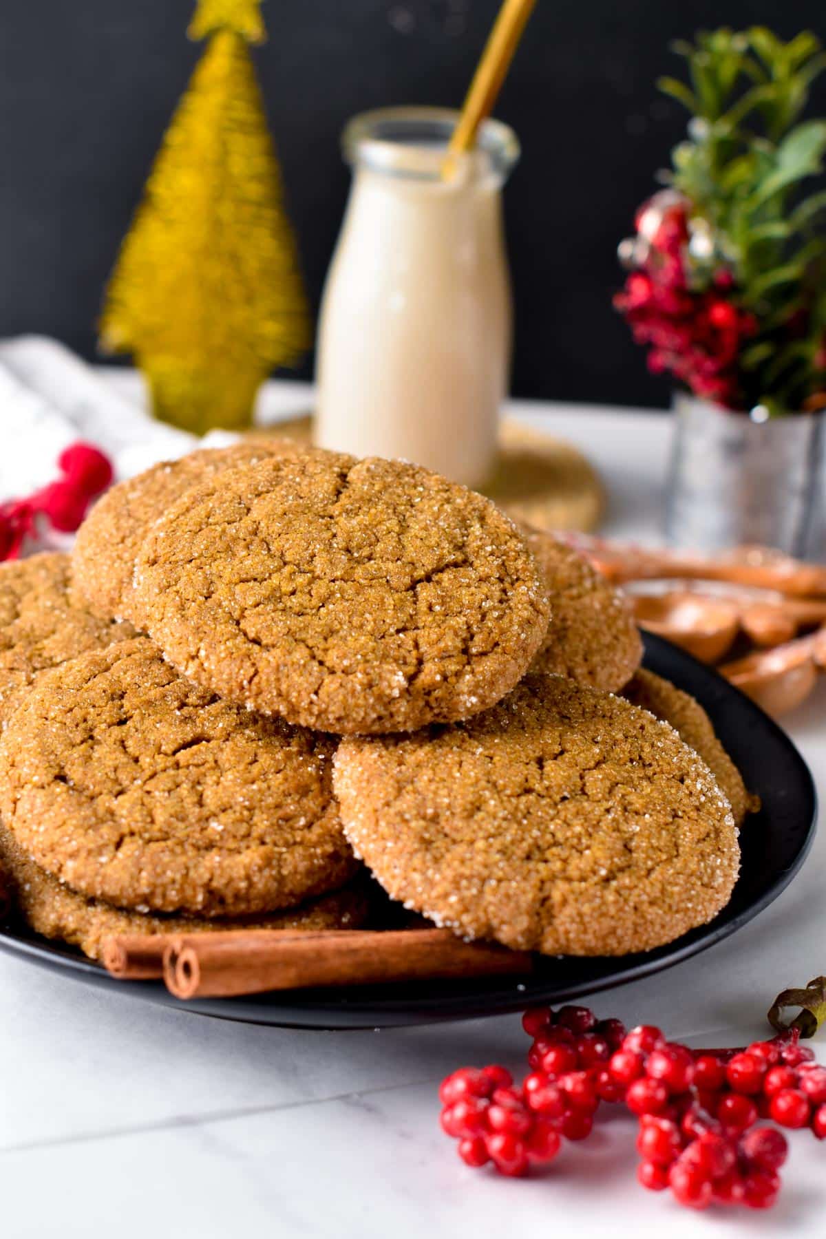 A stack of Vegan Gingersnap Cookies on a black plate with Christmas decor.