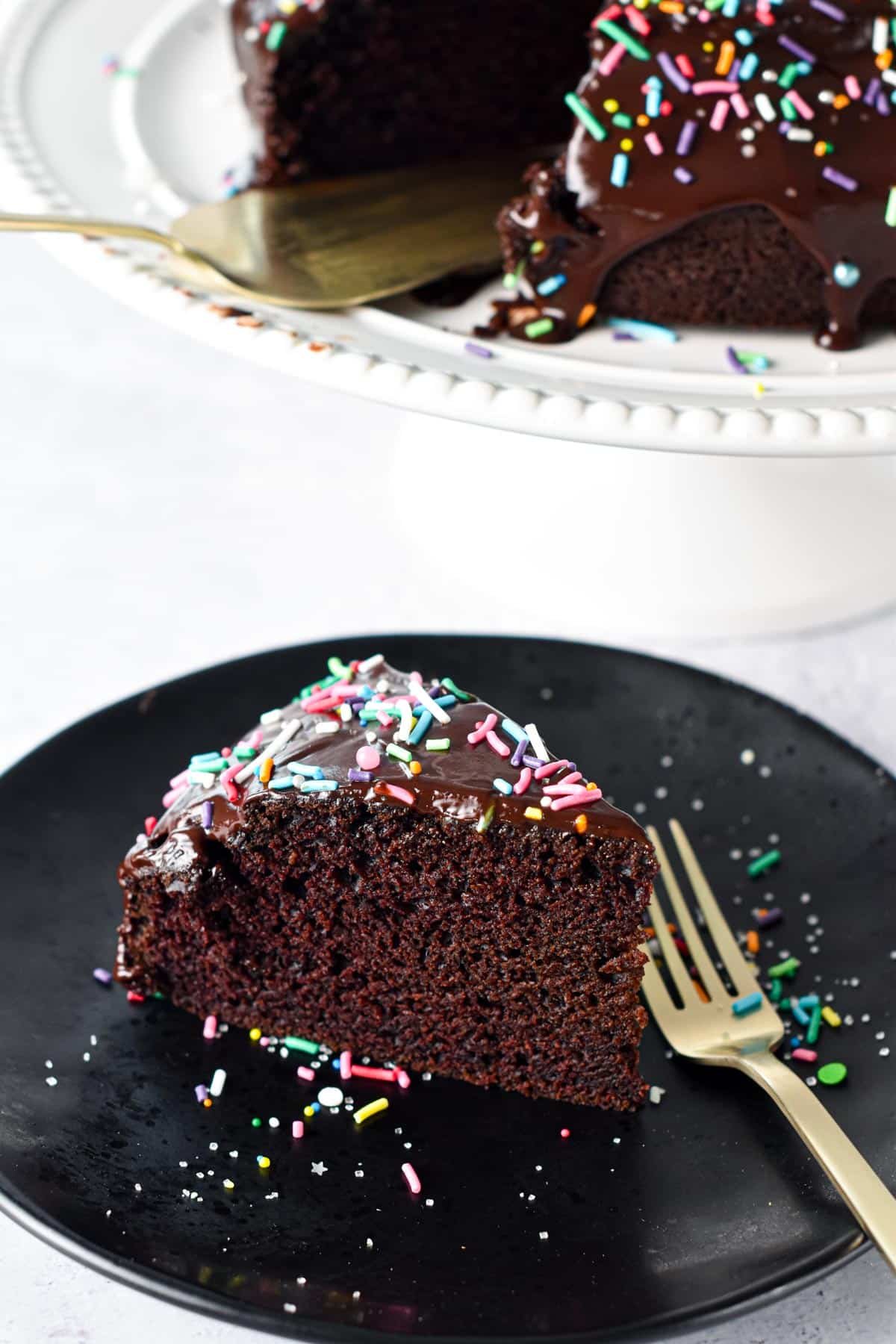 Eggless chocolate cake slice on a black dessert plate with a golden fork.