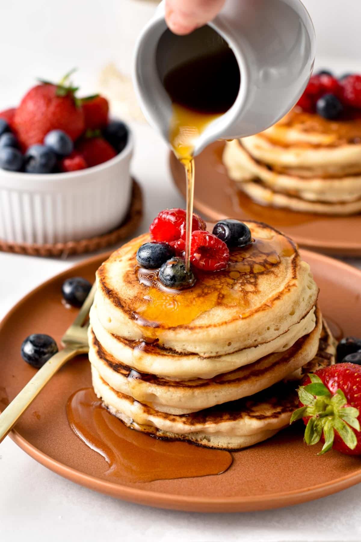 Eggless pancakes on a brown plate with raspberries, blueberries, and maple syrup.