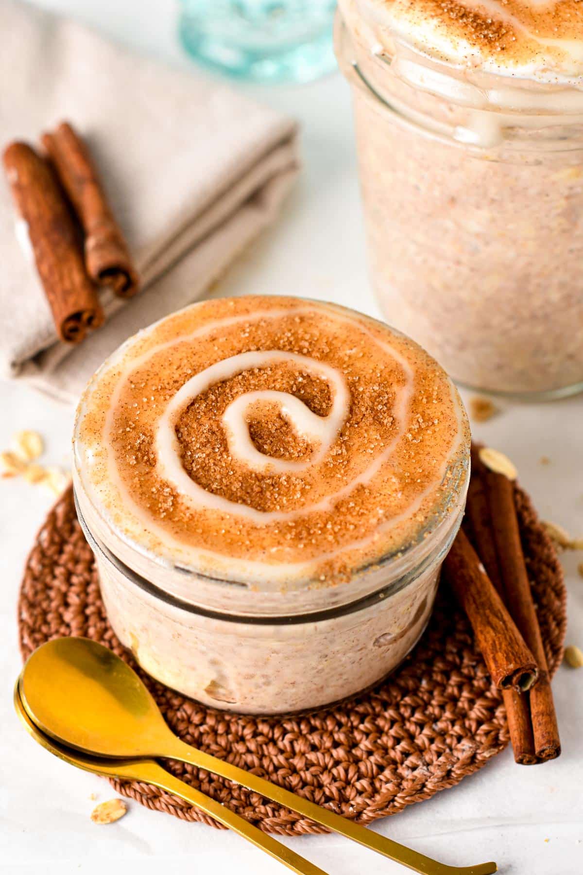 Cinnamon Roll Overnight Oats in a large jar next to two golden spoons.