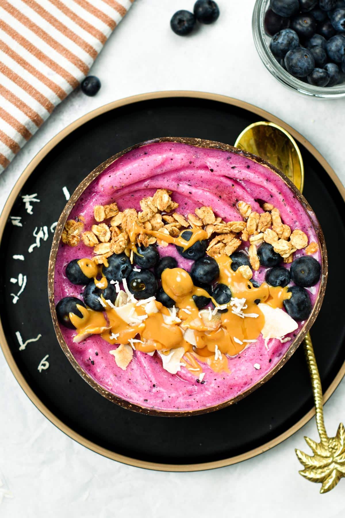 Pitaya bowl decorated with toasted oats, blueberries, peanut butter, and coconut on a coconut bowl.