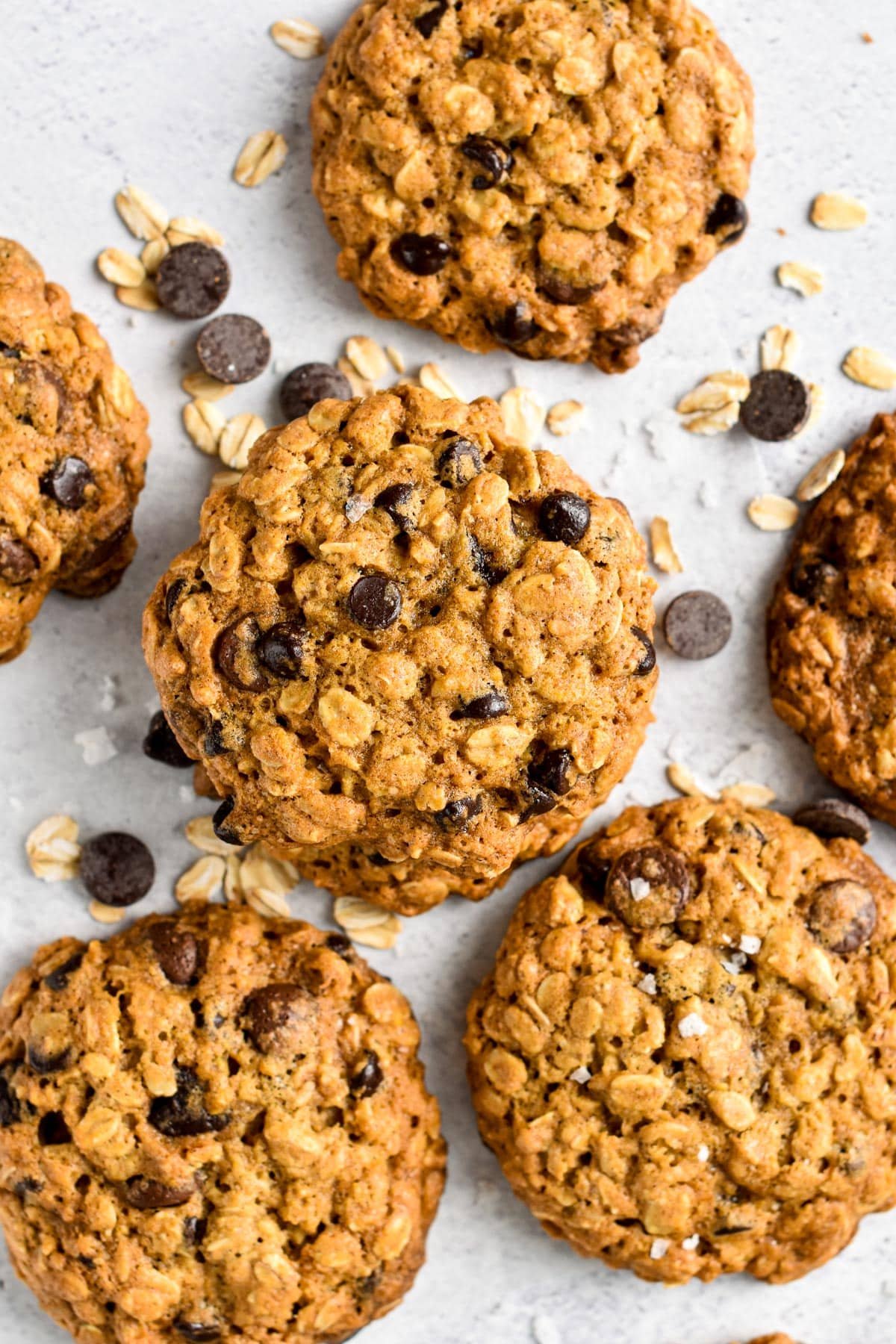 Vegan Oatmeal Chocolate Chip Cookies on a white tablecloth sprinkled with chocolate chips and oats.