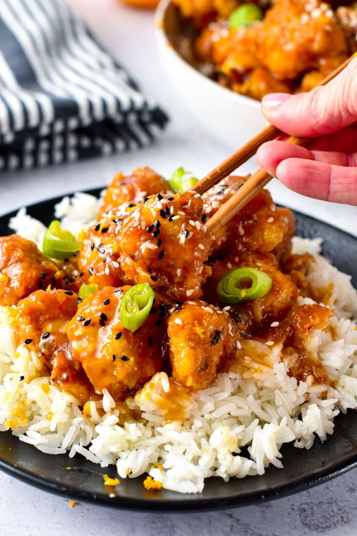 Orange Cauliflower served on top of rice with chopstick holding one floret.