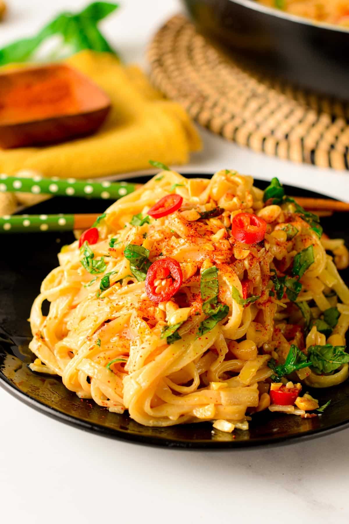 Peanut noodles served on a black plate with chopsticks.