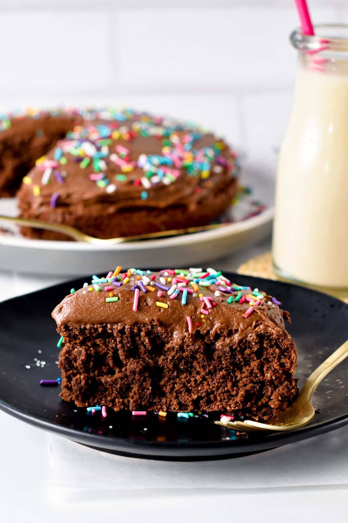 A slice of Protein Cake decorated with sprinkles on a black plate with a golden fork.