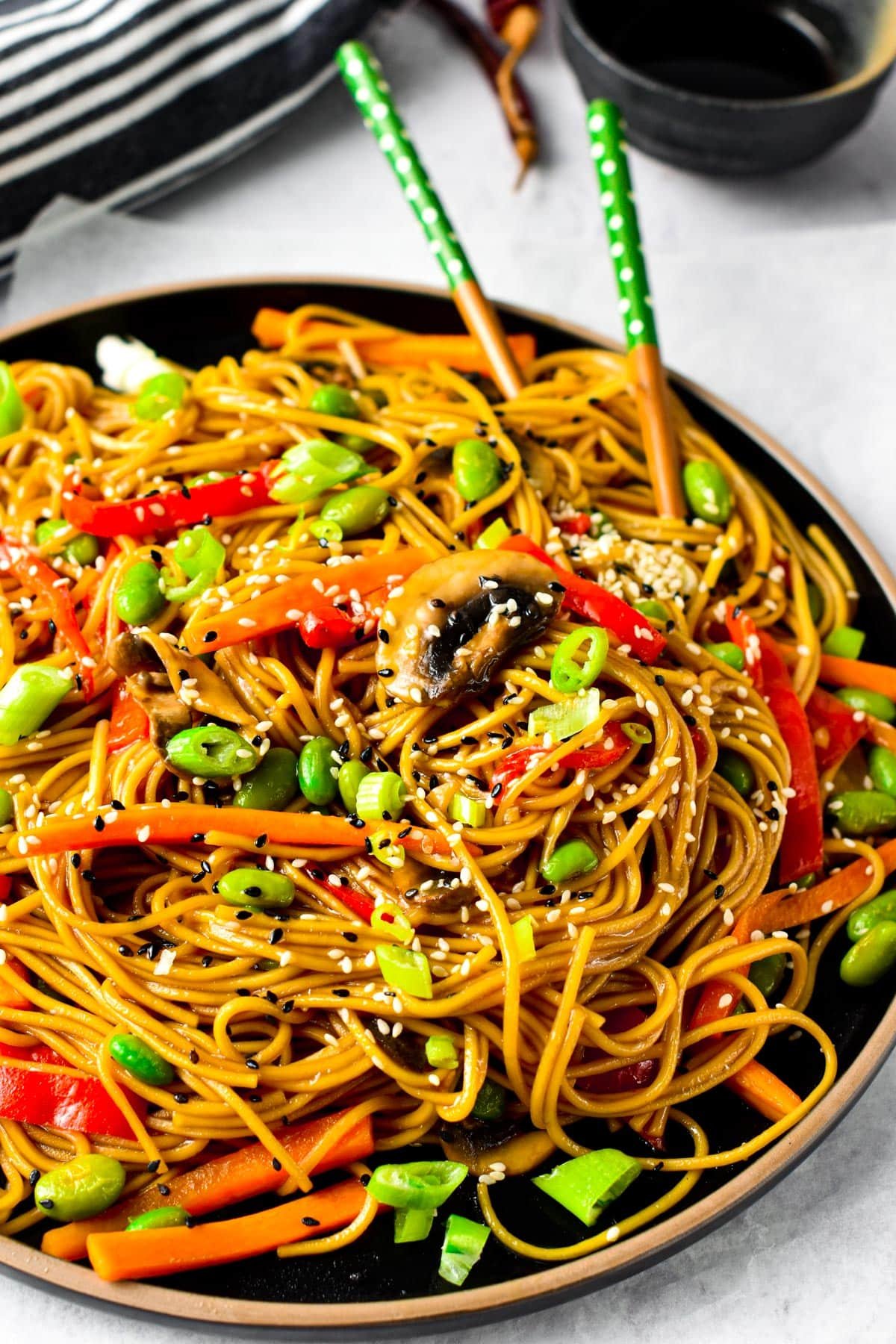 Teriyaki noodles served on a black plate with chopsticks.