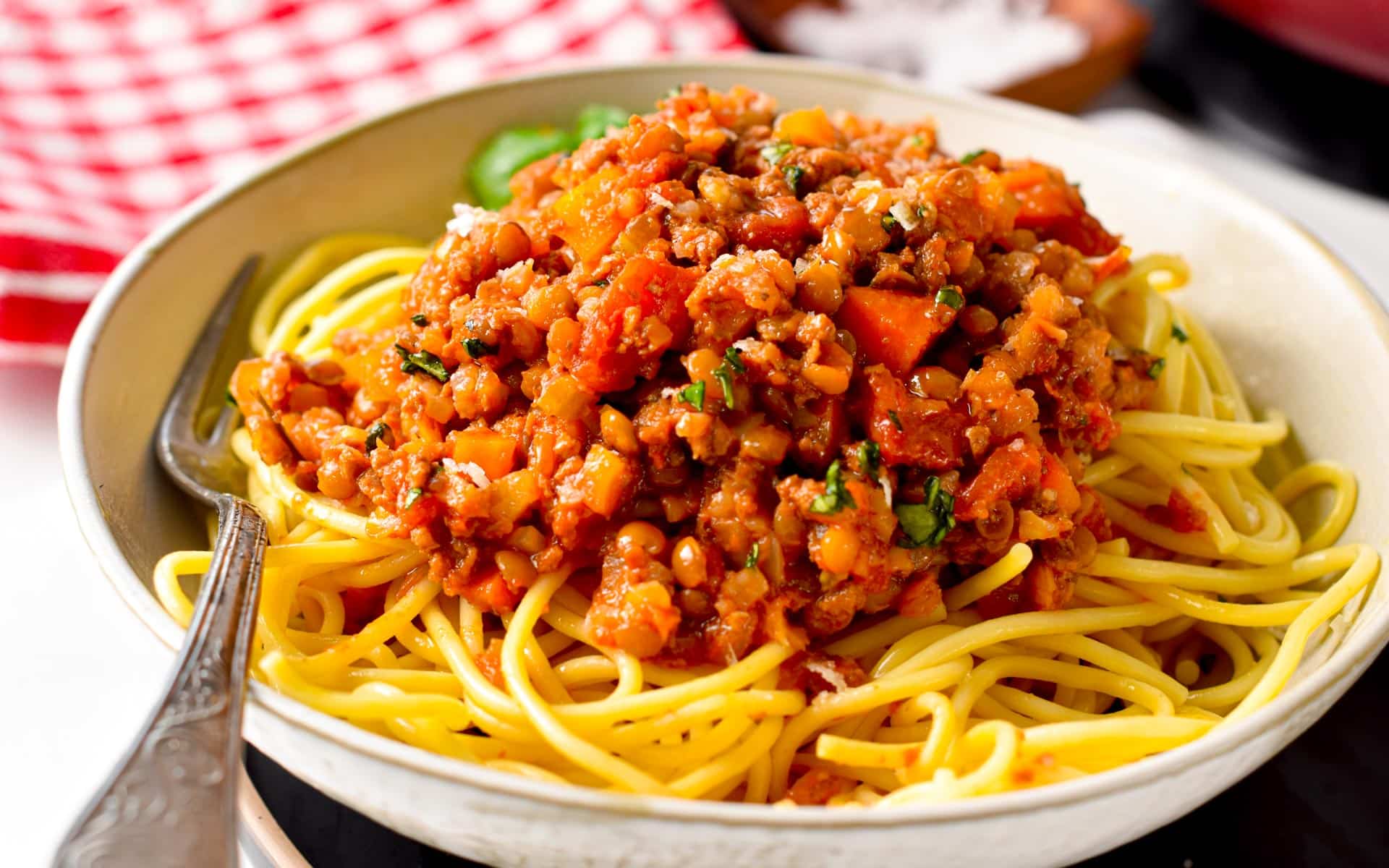 Vegan Bolognese sauce on cooked spaghetti in a large plate with a silver fork.