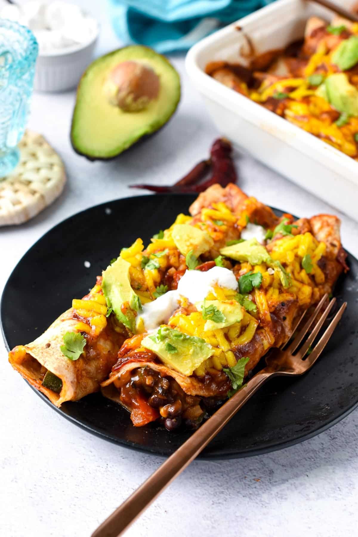 Vegan Enchiladas on a black plate with a golden fork.