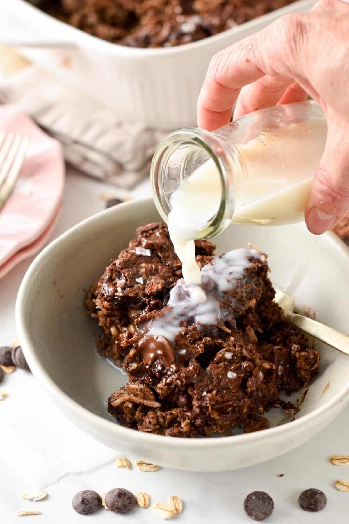 Pouring milk on a portion of Brownie Baked Oatmeal served in a bowl.